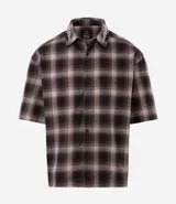 Camisa de corte boxy confeccionada en algodón, con diseño de cuadros escoceses y detalle de lettering bordado en el cuello. Presenta cuello camisero, mangas cortas y cierre frontal con botones.