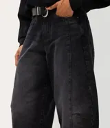 Pantalón baggy balloon de jean negro, de tiro medio con bolsillos delanteros y traseros, recortes estructurales y botamanga ajustada. Incluye cinto de poliuretano con hebilla metálica.