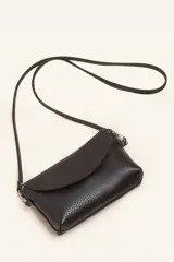 Cartera tipo sobre de cuero color marrón, con solapa frontal redondeada que presenta un detalle circular grabado. Incluye correa larga ajustable y extraíble, cierre principal y broche de seguridad.