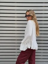 Blusa blanca de textura arrugada, con escote en V y lazos para anudar. Presenta mangas largas con puños acampanados y un diseño con volado en el ruedo.