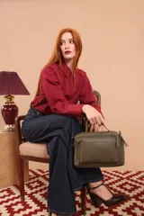 Bandolera de diseño rectangular en color suela, confeccionada en material sintético. Cuenta con un asa superior fija, correa larga ajustable y extraíble, y dos bolsillos frontales con cierre metálico, uno de ellos con diseño superpuesto. Presenta el logo de la marca grabado en el frente.