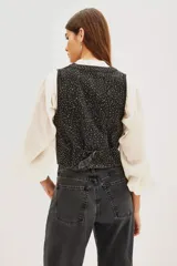 Chaleco de algodón negro con diseño de chaleco de vestir, cuello en V y cierre frontal con botones. La tela está completamente adornada con pequeños apliques brillantes que simulan un efecto de estrellas o puntos de luz.