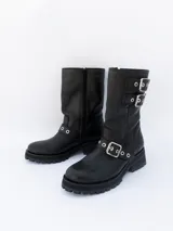 Bota de cuero negra con caña media, suela track y hebillas metálicas.