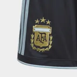 Short de fútbol Adidas de la Selección Argentina, color azul oscuro con tres estrellas doradas y escudo de la AFA en dorado. Presenta tres franjas laterales en color celeste claro y ribetes celestes en los bordes.