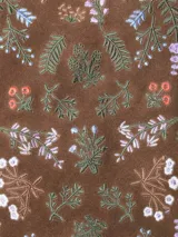 Bolso tipo tote bag confeccionado en cuero serraje color marrón, con diseño artesanal que incluye bordados florales coloridos en el panel frontal. Cuenta con asas de hombro y cierre superior.