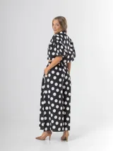 Conjunto de dos piezas con estampa polka dots en negro y blanco, compuesto por un pantalón tipo culotte de tiro alto con bolsillos y una blusa estilo camisa con mangas globo y cierre frontal de botones.