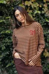 Remerón de manga larga con diseño de rayas horizontales finas en tonos tierra. Presenta un corte holgado y cuenta con un bordado artesanal en color rojo en el pecho.
