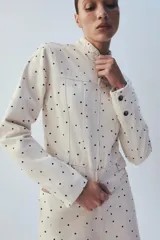 Chaqueta entallada de cuello redondo y manga larga, con cierre frontal de cremallera y falsos bolsillos de solapa en el delantero. Presenta un diseño estampado de lunares.