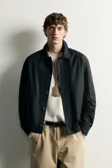 Sobrecamisa negra de corte relaxed fit, confeccionada en tejido de algodón con elasticidad. Cuenta con cuello solapa, manga larga con puño abotonado, bolsillos de vivo en la cadera y cierre frontal de botonadura.