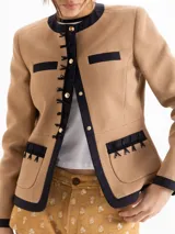 Chaqueta entallada de twill color marrón con detalles en negro que ribetean el cuello redondo, la línea de botones, el ruedo, los puños y los bolsillos. Presenta broches dorados en el frente y las mangas.