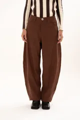 Pantalon de tiro medio con silueta curvada, mas ancha en la zona del muslo y la rodilla, con bolsillos laterales y cierre frontal con cremallera y boton.