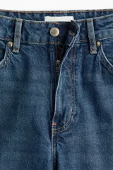 Jean tobillero de denim azul medio, con cinco bolsillos, tiro alto y cierre de botón. Presenta un corte slim fit ajustado en cadera y muslo, con pierna recta.