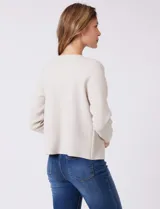 Cardigan tejido de punto color beige, con cuello a la base y cierre frontal mediante un botón metálico decorativo. Presenta mangas largas y corte recto.