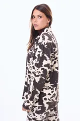 Camisa de denim con estampado animal print tipo vaca en tonos blanco y negro, de corte oversize, con cuello camisero, cierre frontal con botones metálicos y bolsillos con solapa en el pecho.