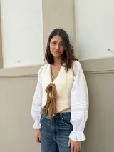 Chaleco de lana color crema con ribetes marrones y lazos frontales.