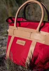 Bolso de playa rojo de lona, con asas y detalles en cuero color tostado. Incluye un parche con el logo de la marca "Sierra Mora" en el frente.