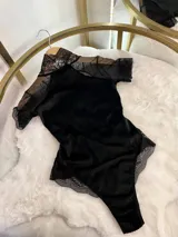 Body de terciopelo acanalado color negro, con cuello alto, mangas cortas de microtul con terminaciones en encaje y espalda descubierta.