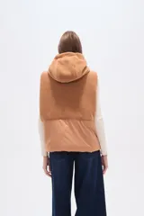 Chaleco negro sin mangas con capucha y cierre frontal. La parte superior es de tejido afelpado (tipo borrego o sherpa) y la parte inferior es de tejido acolchado liso.