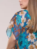 Blusa de gasa semitransparente con hilos de lúrex, diseño estampado floral en tonos blanco, gris y negro, silueta holgada tipo capa y escote redondo con detalle metálico.