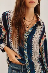 Camisa de manga larga con estampado étnico multicolor, cuello clásico y cierre frontal con botones. Presenta un diseño de rayas verticales con patrones geométricos y detalles en tonos azules, rojos, amarillos y beige.