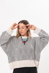 Buzo tejido de punto bicolor en tonos crudo y gris, con silueta relajada, mangas amplias con jaretas regulables en los puños y cuello redondo.