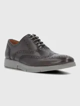 Zapato tipo Oxford o Brogue de cuero marrón oscuro, con puntera y laterales decorados con perforaciones (broguing). Posee cordones grises y una suela deportiva gruesa de goma color gris claro.