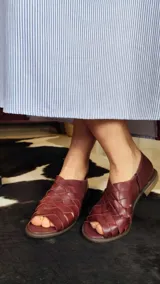 Sandalias de cuero bordó con diseño de tiras cruzadas y entrelazadas en la parte frontal, talón cerrado y suela plana de goma.