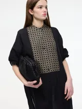 Vestido túnica camisera color negro con botones en la parte delantera, cuello mao y detalle de bordado en el pecho y mangas. Presenta tajos verticales laterales.