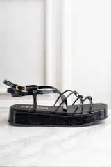 Sandalias negras de cuero charol con plataforma y tiras finas cruzadas.