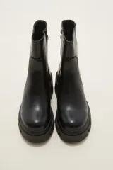 Bota de caña media en cuero sintético color negro, con suela track dentada y cierre lateral interno.