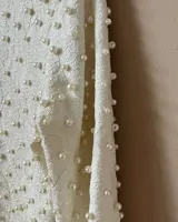 Top corto color crema, de manga media, con espalda baja y cuello bateau confeccionado en tela stretch. Textura de perlas salpicadas aplicadas a mano.