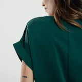 Blusa verde esmeralda de mangas cortas con doblez, escote en V y cierre frontal con cremallera dorada.