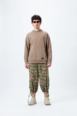 Canguro marrón con capucha, bolsillo frontal y puños ajustados. Estampa frontal con la palabra 'Dramatic' y gráfico en la espalda con tipografía bold y serpiente ilustrada.