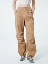 Pantalón color marrón claro, de corte ancho, con elástico en los tobillos, cierre central con botón y bolsillos delanteros.