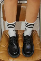 Zapato acordonado de estilo borcego en color negro con acabado charolado, suela track dentada y costuras blancas visibles en el borde de la suela.