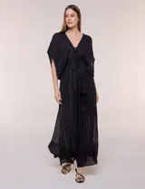 Vestido largo negro confeccionado en gasa con hilos de lurex en relieve vertical. Presenta escote en V profundo con lazo frontal y borlas, mangas holgadas tipo kimono, cintura elastizada y falda fluida con ruedo con volante.