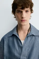 Camisa polo de calce relajado confeccionada en tejido de lino color azul. Presenta cuello solapa con abertura frontal en V y manga corta.