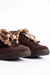 Zapatillas urbanas de gamuza color marrón, con diseño de cordones decorados con cuentas de piedra y detalles de líneas brillantes en los laterales. Presentan suela de goma texturizada al tono.