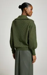 Sweater de punto color verde militar, con cuello polo y escote en V, mangas largas abullonadas con puños ajustados y tejido con tramas geométricas combinadas.