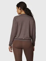 Polera de manga larga en color marrón chocolate con efecto melange. Presenta cuello redondo, mangas raglán, puños elásticos y cintura con ajuste elástico. Incluye un pequeño logo bordado en el pecho.