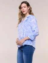 Blusa celeste con estampado efecto pincelada blanca, de corte semi holgado, escote en V con cuello solapa y media abotonadura frontal con botones nacarados. Presenta finas alforzas verticales en la pechera y mangas 3/4 con puños elastizados.