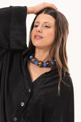 Camisa negra plisada de manga larga con puños vueltos, cuello camisero y cierre frontal de botones claros.