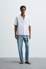 Camisa de algodón con rayas verticales finas azules y blancas, corte relajado (relaxed fit), cuello bowling y manga corta. Posee un bolsillo plastrón en el pecho y aberturas laterales en el bajo.