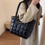 Bolso tote negro con diseño acolchado y cierre de cremallera. Tiene dos asas de hombro y un bolsillo frontal con cierre.