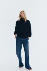 Buzo de punto fino en color azul marino, con cuello alto acanalado, mangas tres cuartos y hombros caídos. Presenta terminaciones acanaladas en puños y ruedo.