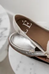 Mocasines de cuero color dorado con acabado texturizado, diseño clásico de punta redondeada y costuras visibles en el empeine. Cuentan con suela plana y flexible.