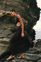 Vestido midi de color negro, sin mangas, con cuello redondo y aberturas laterales en la cintura (cut out). La parte superior es de punto liso y la falda presenta una textura plisada y ligera.
