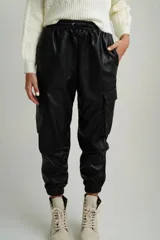 Pantalón babucha negro de cuero sintético con cintura elastizada con cordón ajustable, bolsillos laterales y bolsillos tipo cargo con solapa en los laterales de las piernas.
