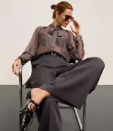 Pantalón de sastrería de corte recto y tiro alto, con diseño de pierna ancha, trabillas en la cintura, cierre frontal con botón y cremallera, y bolsillos laterales con costuras verticales.