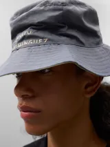 Gorro tipo bucket gris con banda decorativa y texto bordado.